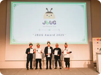 Backlog World のプログラムにあるGood Project 「JBUG Award 2025」の授賞式。壇上の大きなスクリーンの前で、表彰状を手にした5人の受賞者が並んで記念撮影をしている。