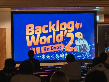 会場の後方からの写真。Backlog Worldのロゴがスクリーンに投影されている