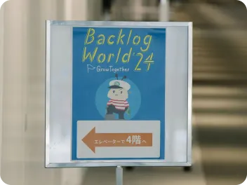 BacklogWorld 2024の看板。エレベーターで4階へ移動する案内が書かれている。