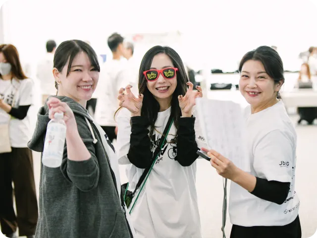 イベント会場で笑顔を見せる3人の女性。中央の女性はBacklog Worldのサングラスをかけてポーズをとっている。